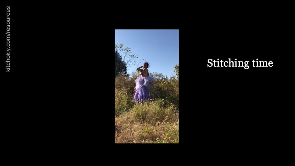 Again a new still, this time with only one frame. It is in high-resolution and again in a vertical aspect ration. The figure stands in a field wearing a gauzy purple dress which leaves their chest revealed, although their arms cover them in this moment. Their hair is pulled back. "Stitching time" remains.