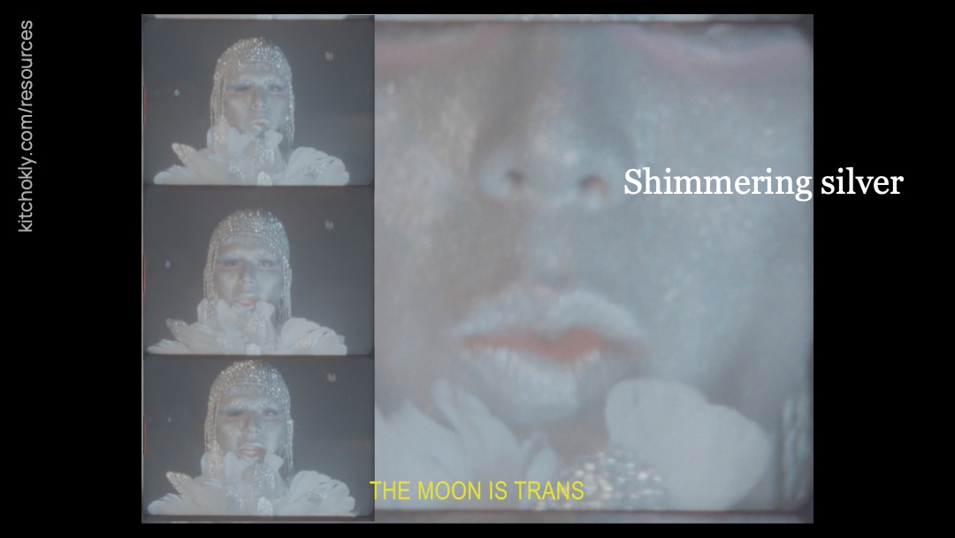 The still includes three nearly identical shots of the figure as a portrait, who is painted entirely in silver. They are neatly stacked one on top of the other on the left-hand side of the shot. The rest of shot is a close-up on the figure's lips, which are mouthing along to the subtitles. These subtitles are now in all capitals and read "THE MOON IS TRANS". "Stitching time" is replaced with "Shimmering silver".