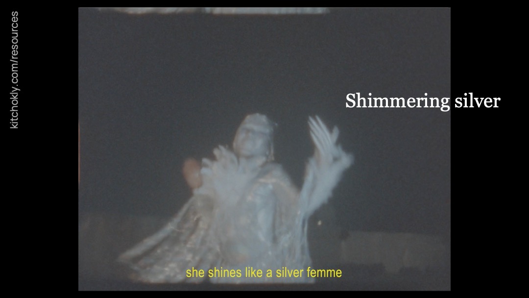 This shot includes one, full-screen frame of the figure in silver. They are twirling in their silvery outfit, their hands in the air and blurred by motion. The yellow subtitles, back to all lowercase, read "she shines like a silver femme". "Shimmering silver" remains.
